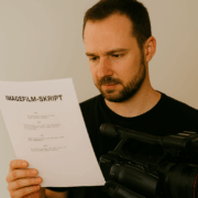 Kameramann liest aufmerksam ein ausgedrucktes Imagefilm-Skript und hält dabei seine Videokamera in der Hand.
