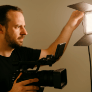 Kameramann mit Videokamera richtet LED-Licht aus, um die Ausleuchtung für eine Szene beim Imagefilm-Dreh einzustellen.