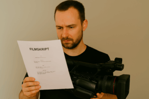 Kameramann hält ein Filmskript in der einen Hand und seine Kamera in der anderen, während er konzentriert das Drehbuch studiert.